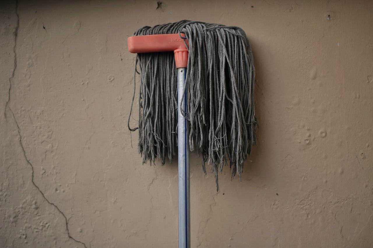 about-02 Gray mop leaning against a textured wall, conveying simplicity in a domestic setting.